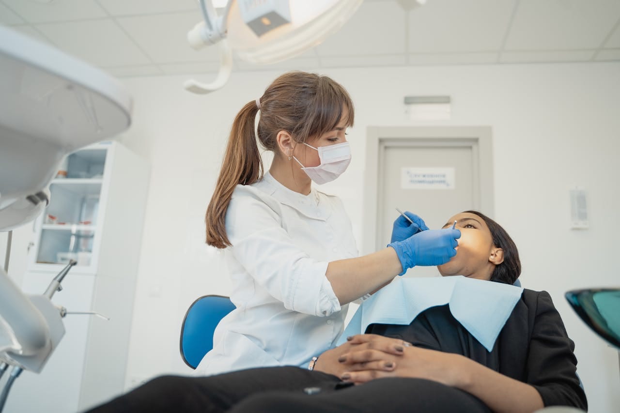 pexels-photo-5355828 A female dentist wearing a facemask examines a patient in a modern dental clinic setting.