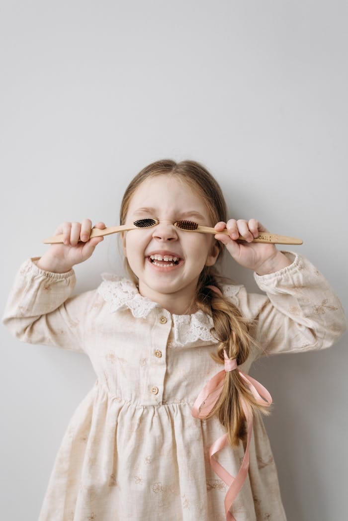 pexels-photo-7055304 A happy child with braided hair playfully holding bamboo toothbrushes in front of her eyes.